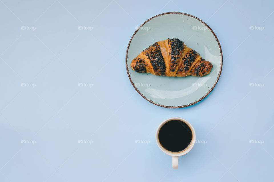 Business working morning with cup of hot coffee, croissant on blue background close up. Top view, copy space, flat lay, mockup.