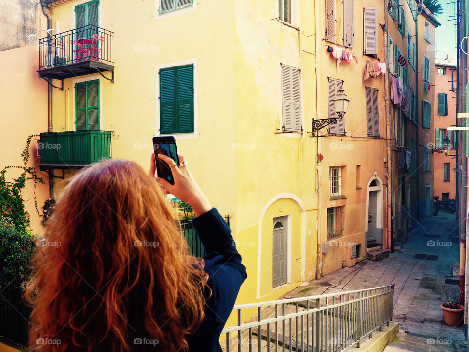 Redhead young woman taking photo with phone in the old town of Nice, France.