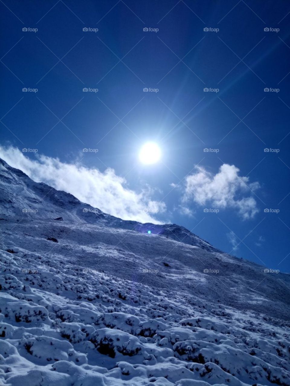 snow covered mountains very beautifully and the sun rises with the rays that fall on the snow and it looks really nice the clouds are travelling with the sun they want to hide the sun