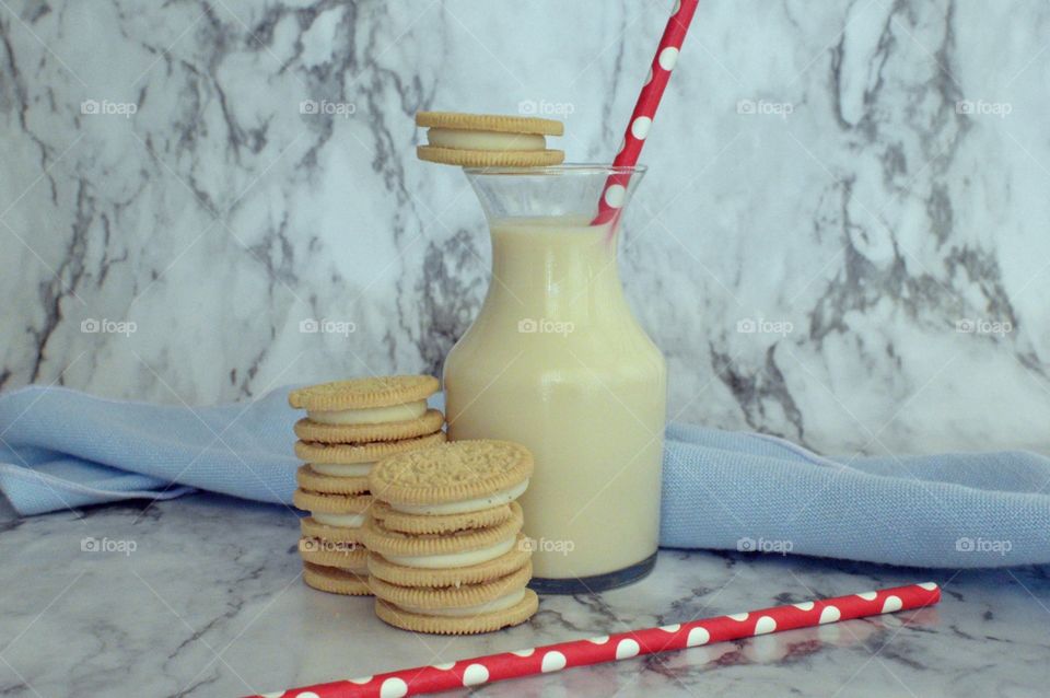 Oreo double stuff cookies stack next to a carafe of milk with a red and white straw on a marble backdrop
