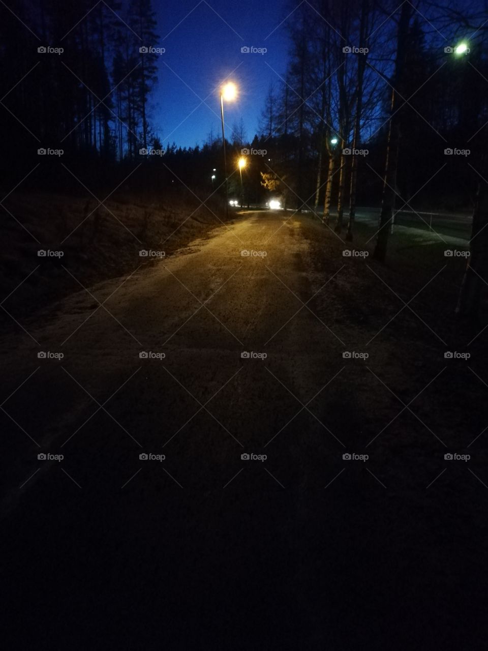 An icy road in the sunset. The lights of the streetlights and the cars are bright. The sidewalk is snowy in the dark.