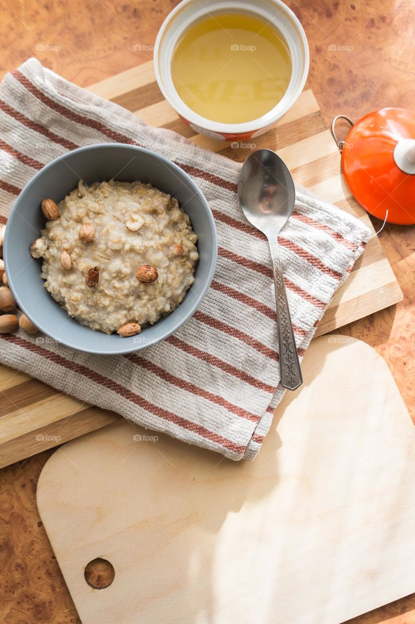 Cooked oatmeal in a deep gray plate with hazelnuts and honey.