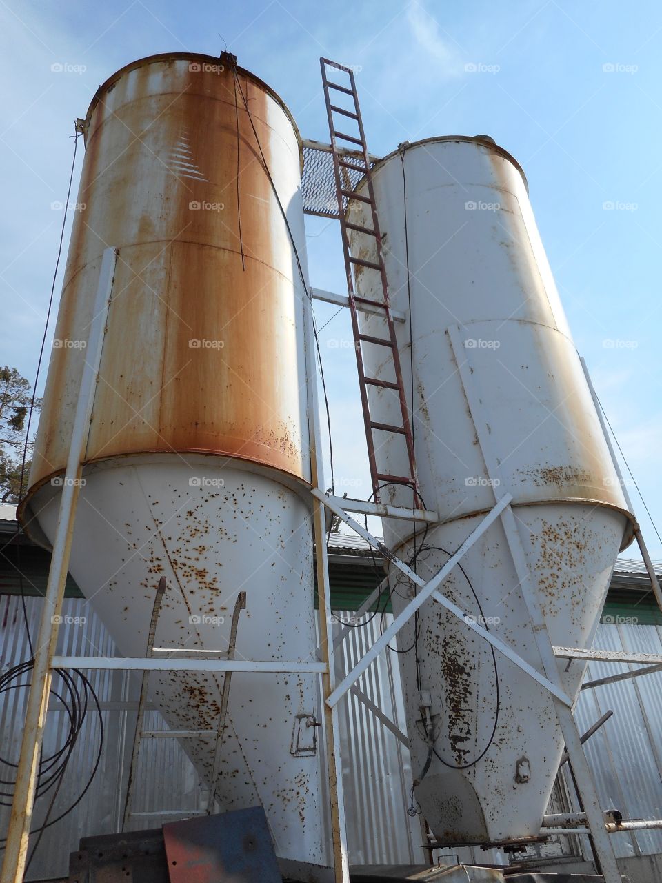 Two rusted old feed silos on a ranch tower into the sky on a sunny summer day