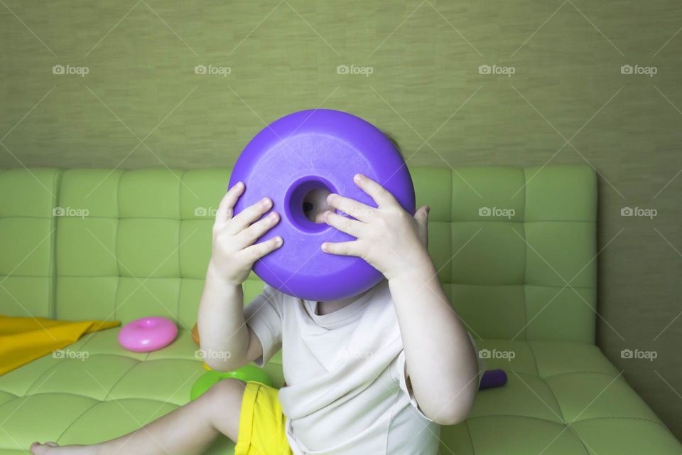 The child is having fun playing a bright pyramid educational toy, sitting on a green sofa.