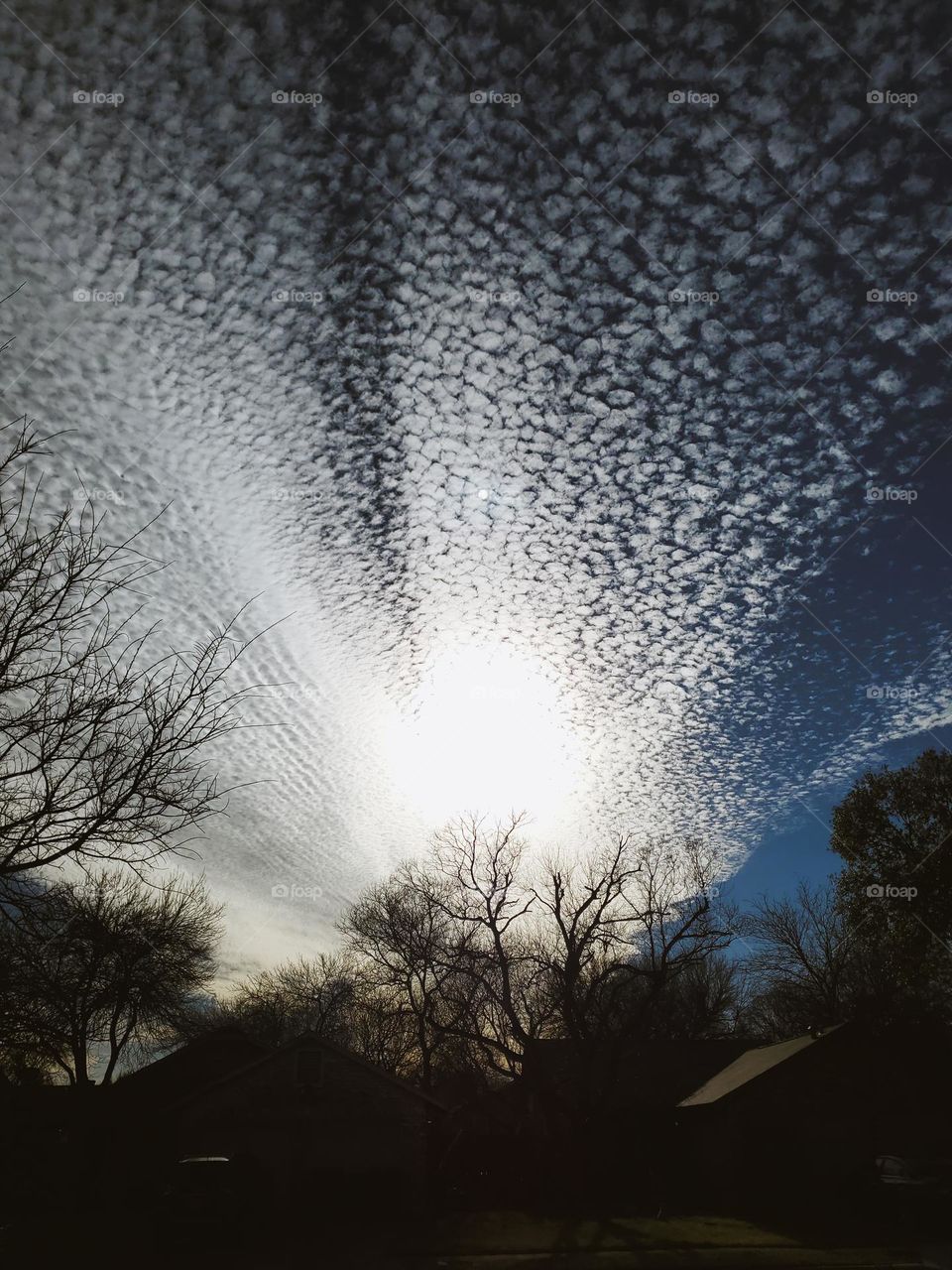 The sun sets behind a row of homes while being covered by a spectacular outburst looking cloud formation leaving the homes and roof tops in the shadows.