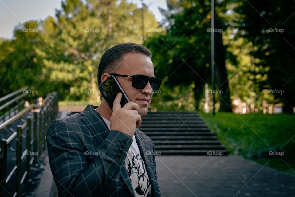 Young man walking in the park in summer, talking on the phone