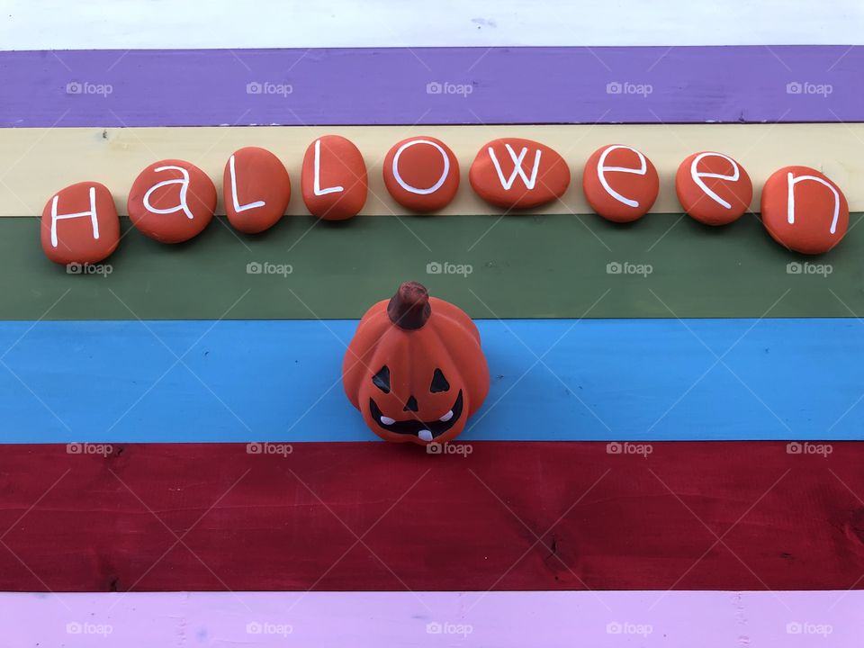 Halloween handmade message with orange painted stones and multicolored wooden board