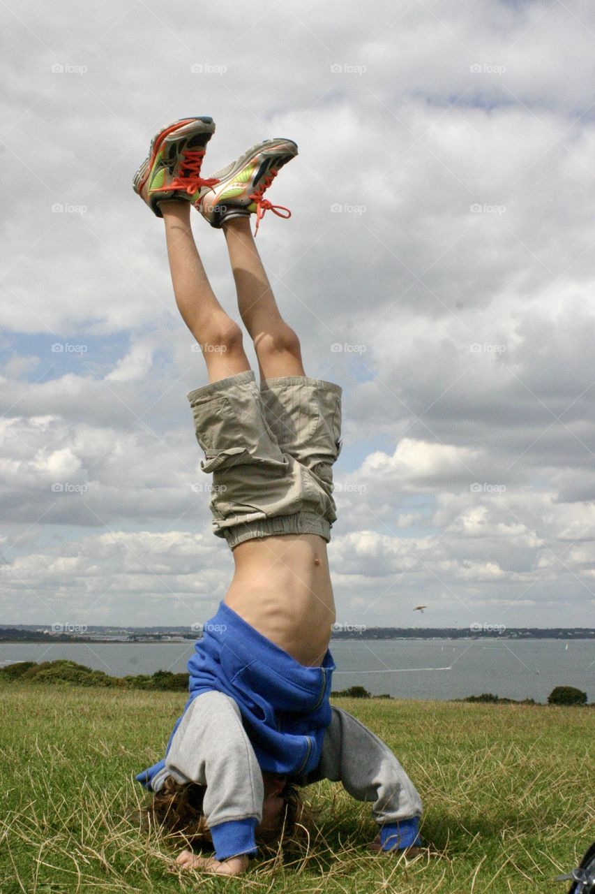 Kid doing headstand on a green grass viewing the sea