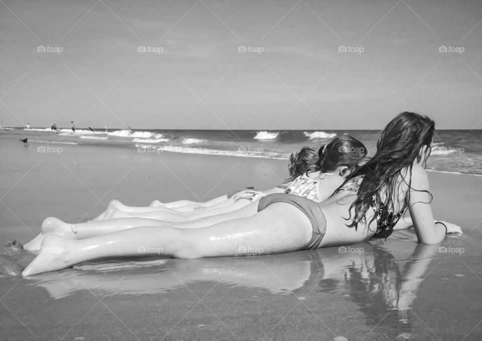 Three girls laying on the beach at the oceans edge watching the waves crash.