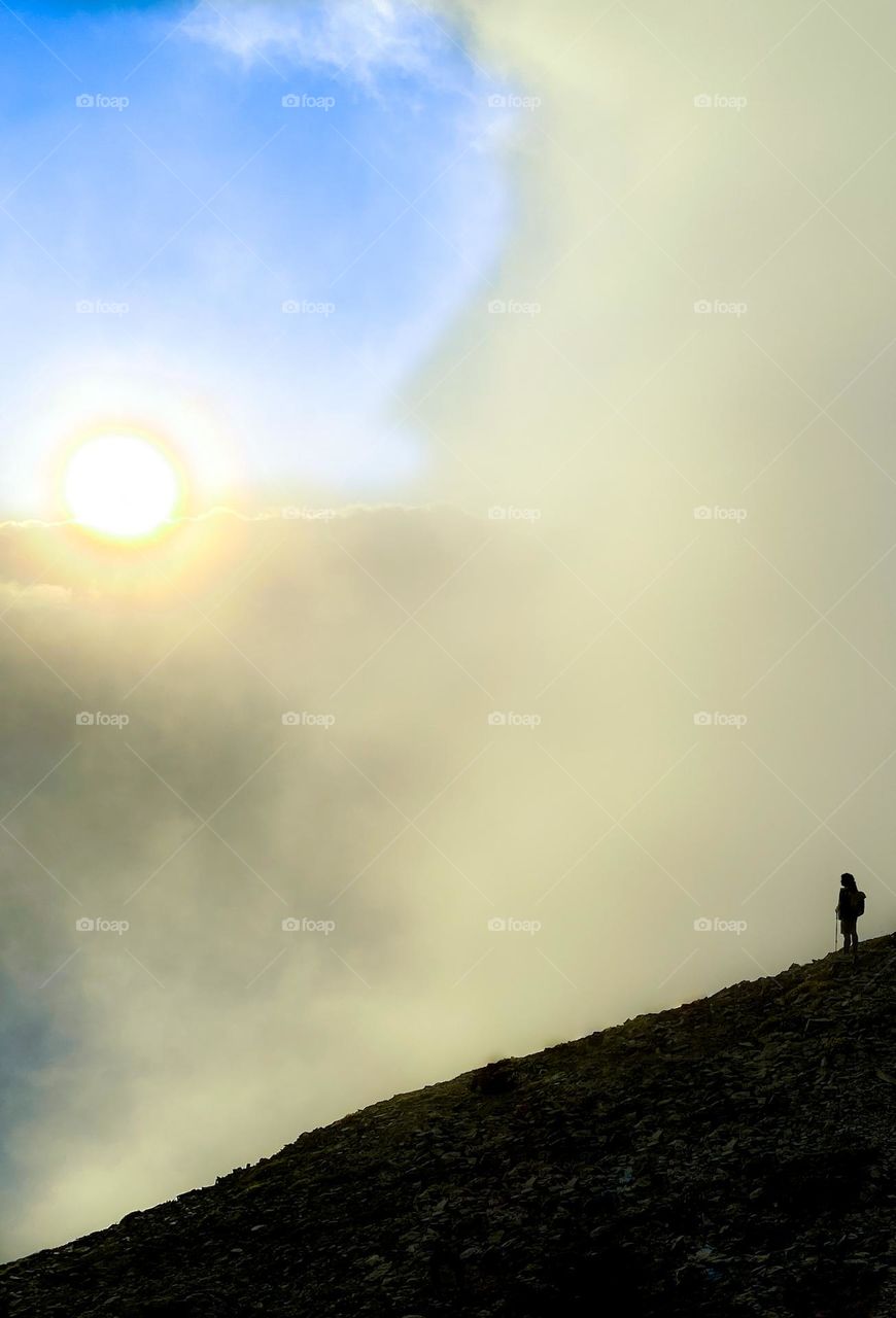 Hiker enjoying the sunset along a high alpine ridge in the Cascade mountain range during a brief clearing in the clouds