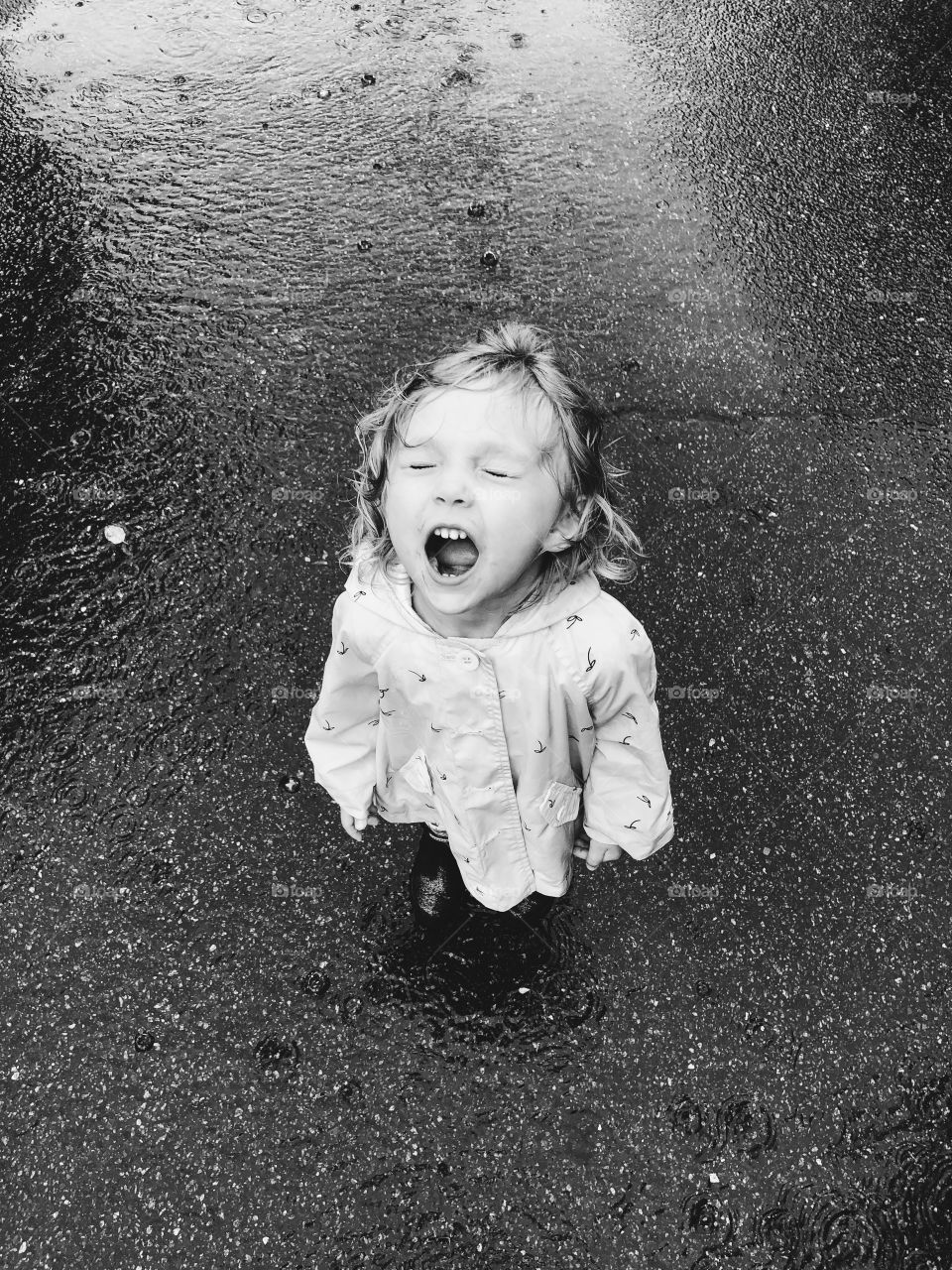 Little girls standing in the rain trying to catch rain drops in her mouth.