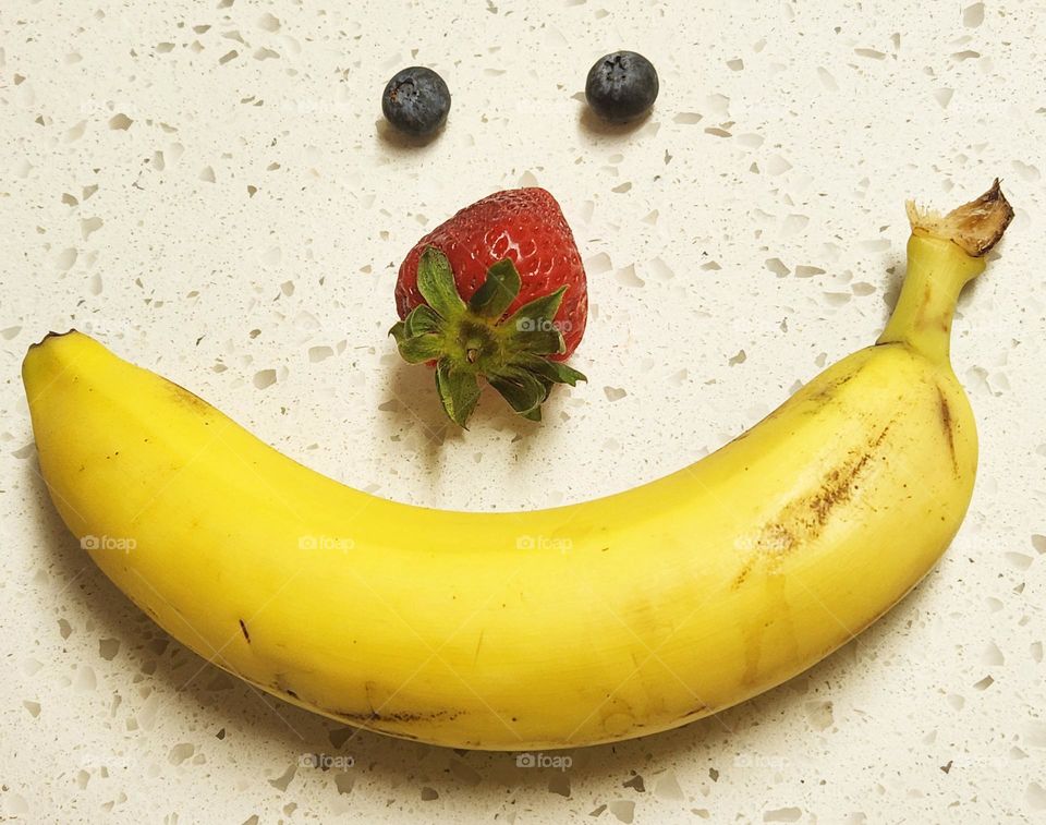 A friendly healthy fruit face made out of blueberries, strawberry, and banana to cheer you up