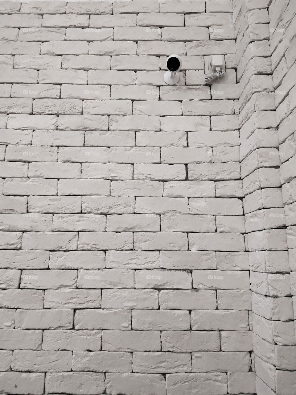 White brick wall on which a black surveillance camera hangs