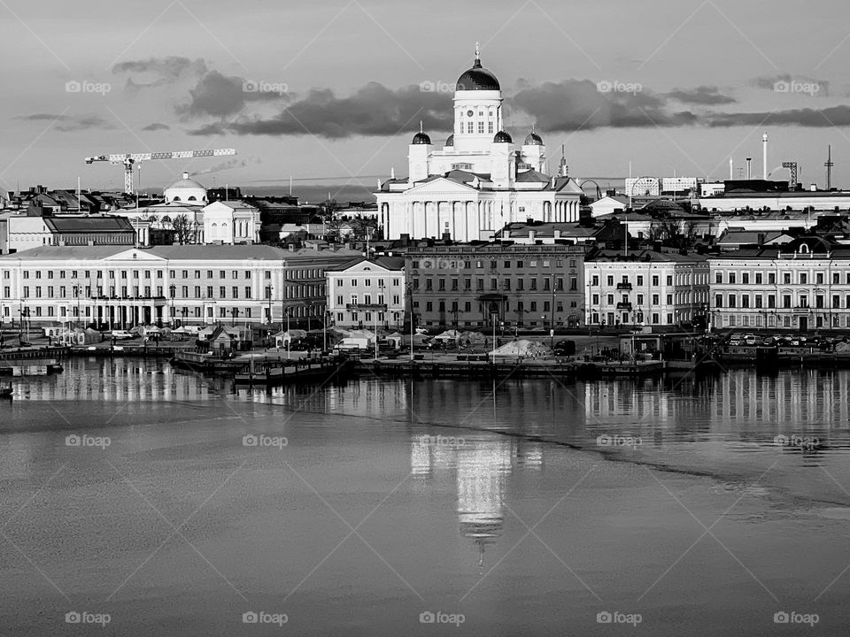 Coastline cityscape of Helsinki with houses, Tuomionkirkko cathedral and reflection in the sea water surface in black&white monochrome 