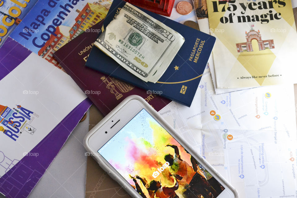 A cell phone with Foap app ,dollars ,passports and travel Maps and brochures
