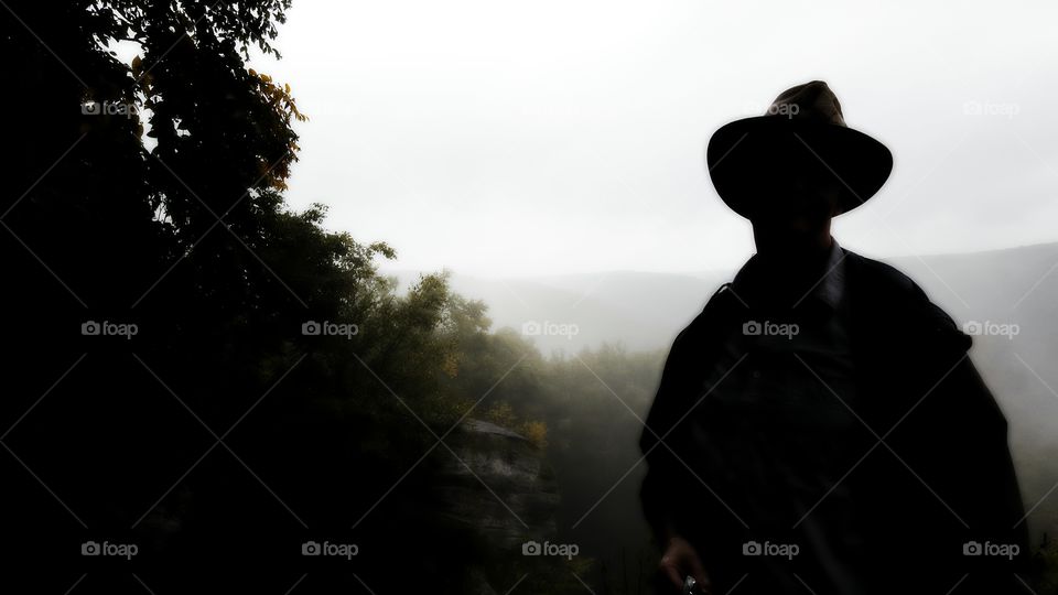 Silhouette of a park ranger during a rainy morning hike standing atop a mountain overlook with the mist hanging in the treetops behind him.