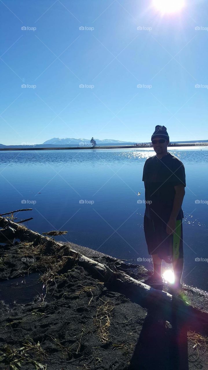 a man silhouetted with Yellowstone Lake in the background and mountains and trees all around. 2017 Yellowstone National Park United States of America