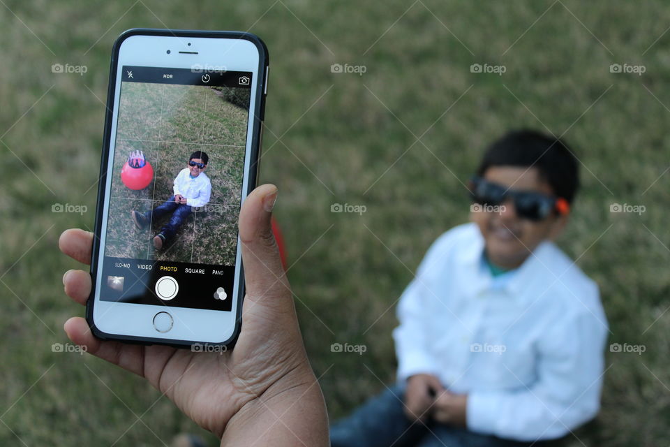 Snapping photo from iPhone and showing  tech screen while kid is sitting in grass in happy mood 