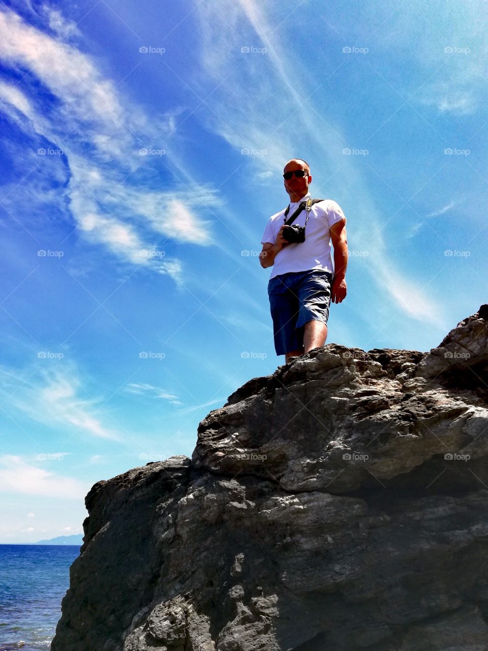 Man standing on a basaltic volcanic rock taking a picture with azure sky above him