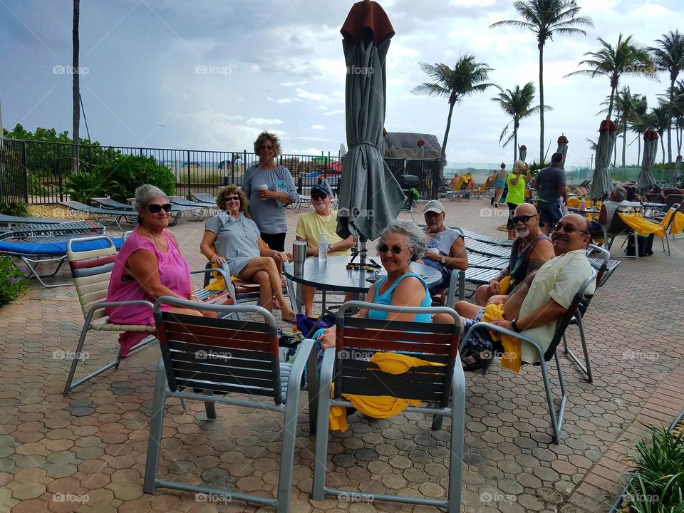 Friends & family sitting around umbrella table at ocean resort just before rain storm. Palms were blowing in the warm wind.