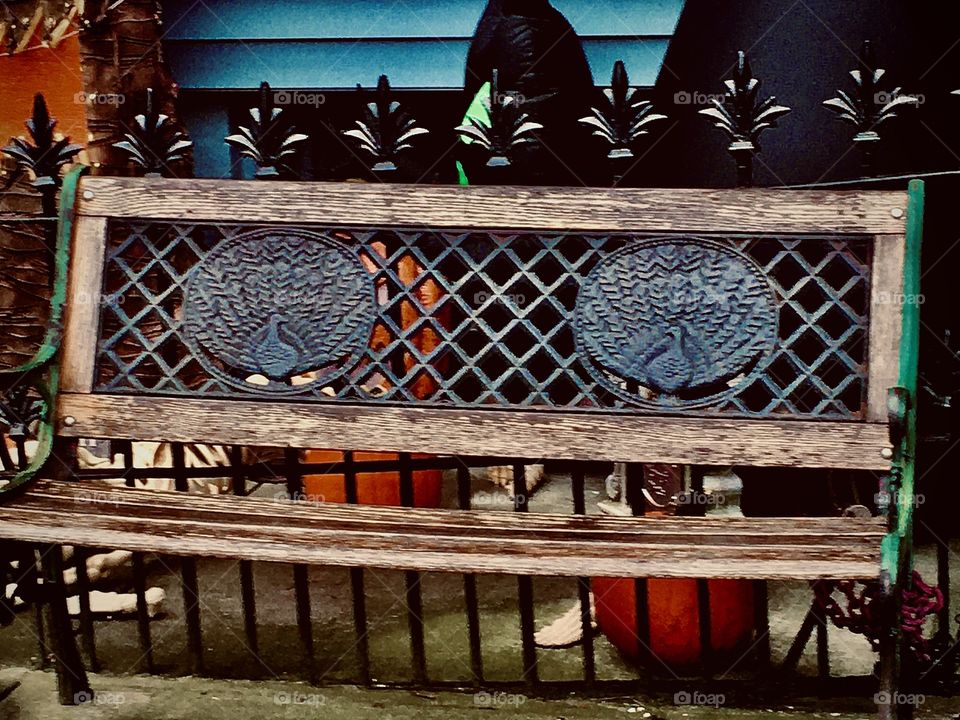 An ornamental cast iron and wood bench on the sidewalk leaning against a cast iron fence with spikes shaped like the commonly known playing card suit of “Clubs” the equivalent of “Pentacles”. Halloween 2020. Hypnotic Productions