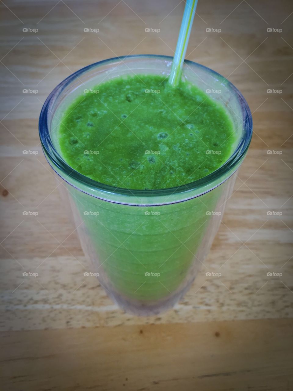 Green smoothie healthy drink in plastic tumbler sitting  on wood table 