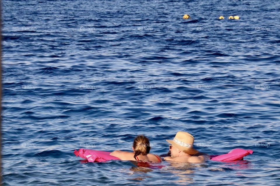 Two women on pink floating mattress in the blue sea