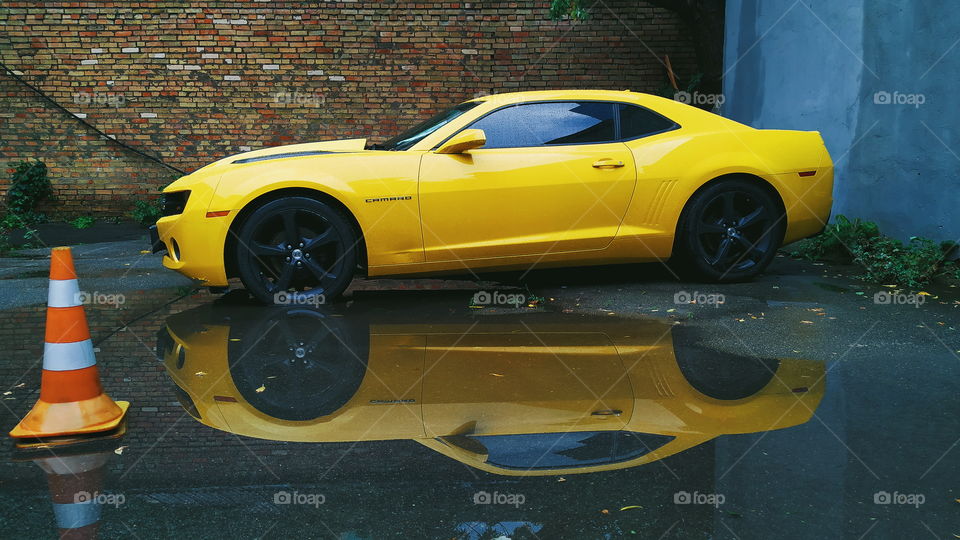 reflection of a yellow chevrolet car in a rain puddle