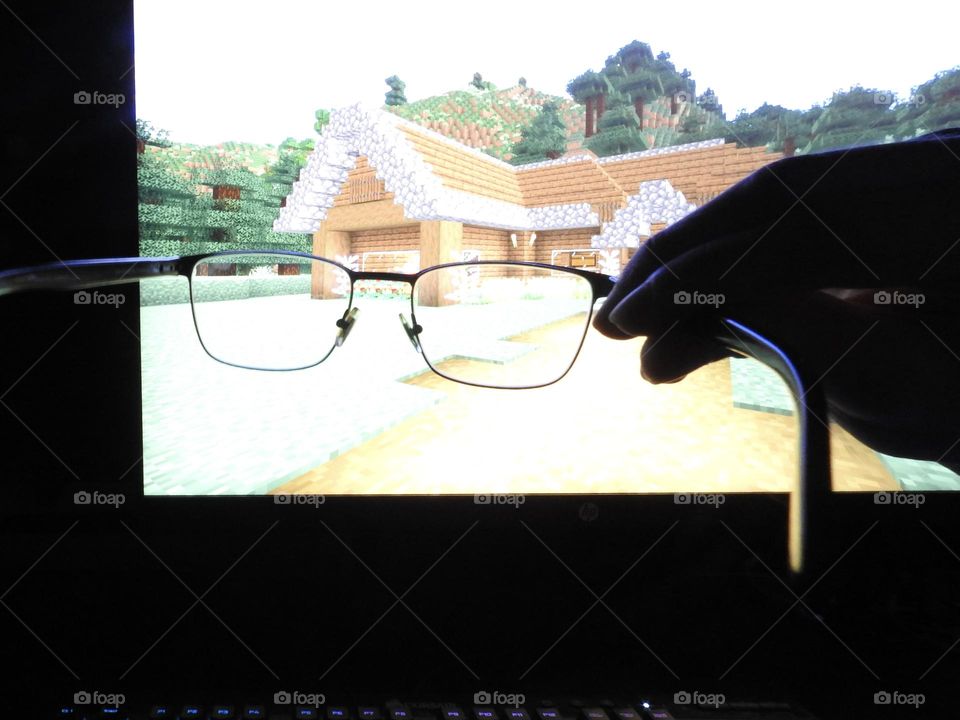 Teenager boy playing Minecraft on the gaming computer seen from his glasses close-up in a dark room.