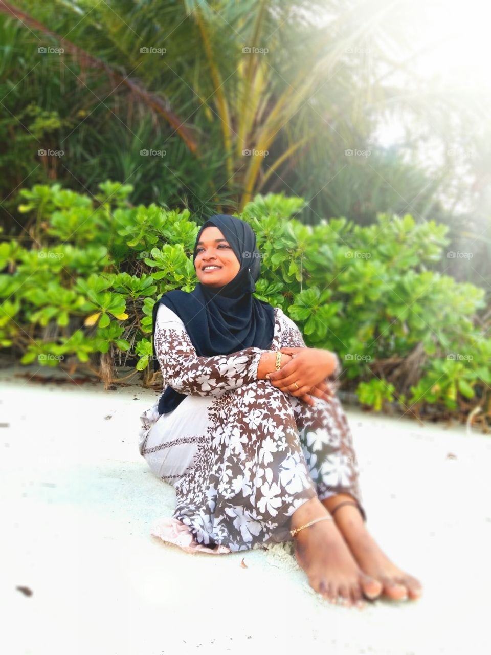 Smiling woman sitting on sand with head scarf