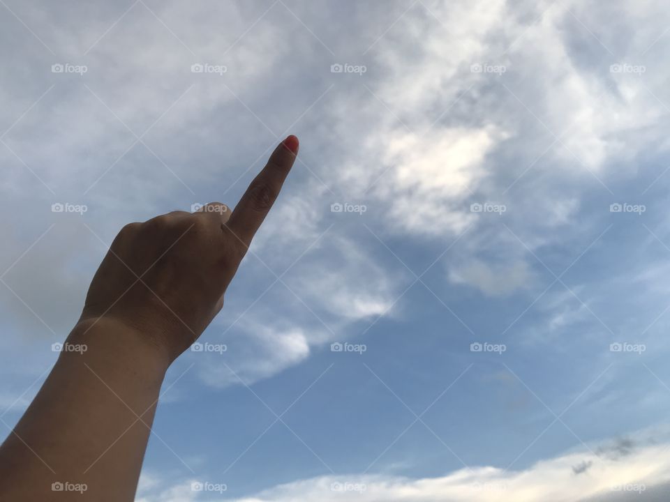 woman uses her left index finger pointing up in the bright blue sky with white cloud in daylight with copy space on the right side of frame
