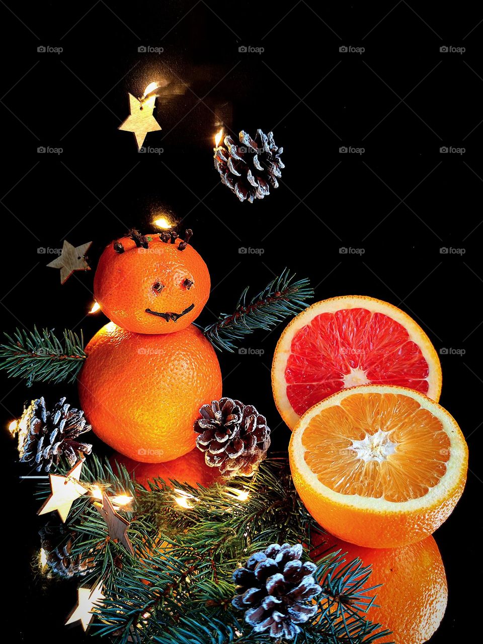 Winter Fruit Tale. Snowman made of tangerines, orange and red orange halves, garland lights, fir tree branch