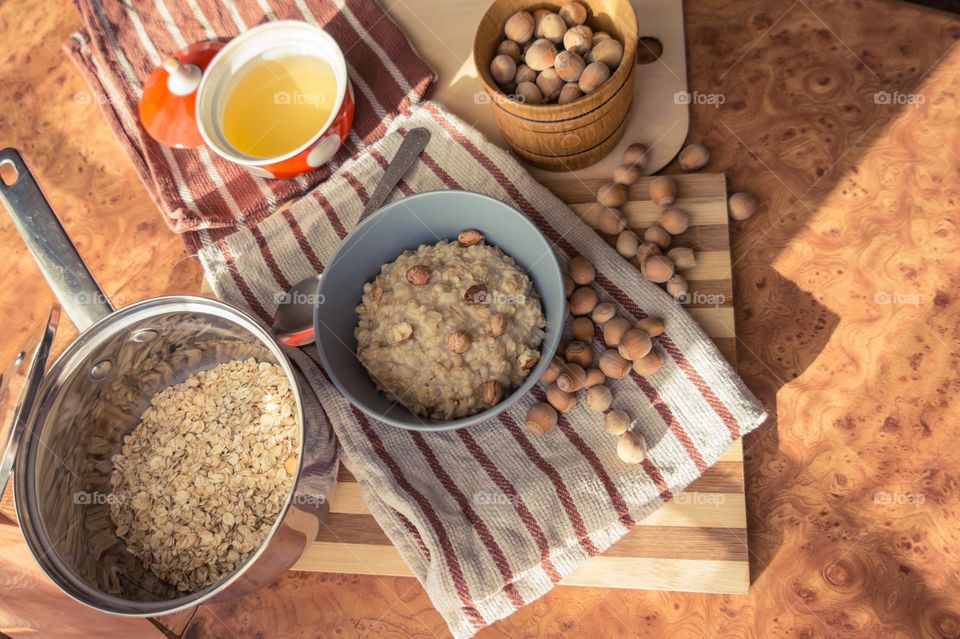 Cooked oatmeal in a deep gray plate with hazelnuts and honey.