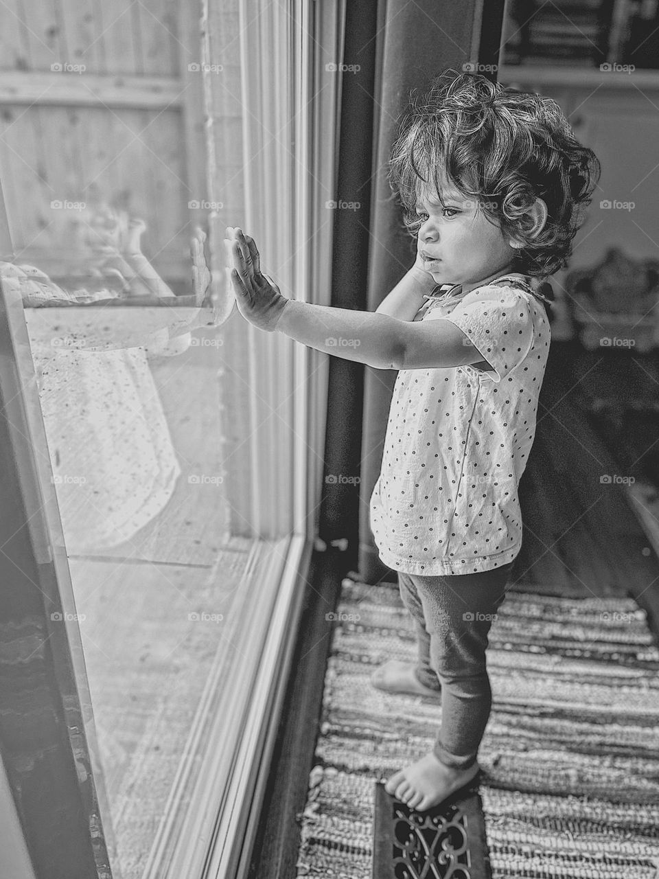 Toddler girl standing at window looking out, monochrome portrait, toddler girl looks thorough glass window, reflection in the window, cute kids in windows, black and white toddler photo, toddler girl looking outside from window