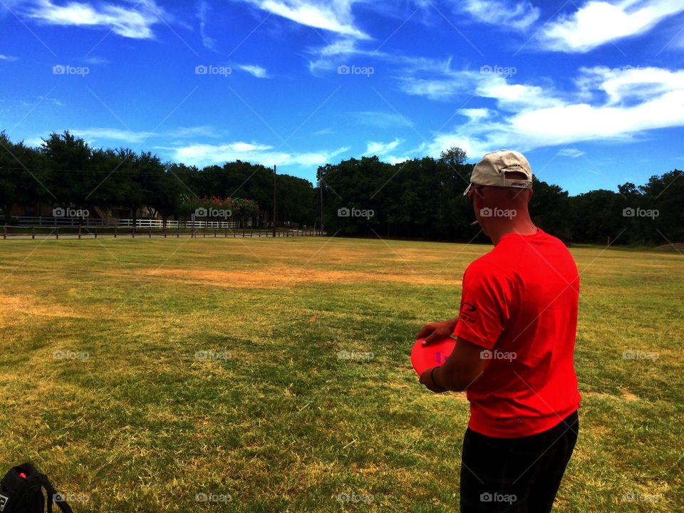 A disc golfer takes aim at a target nestled in the trees on a sunny day in Texas.