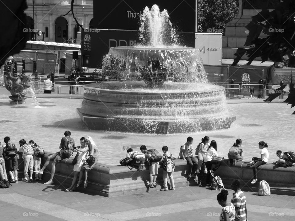A crowd of people gather around a fountain to visit and relax on a hot summer day. 