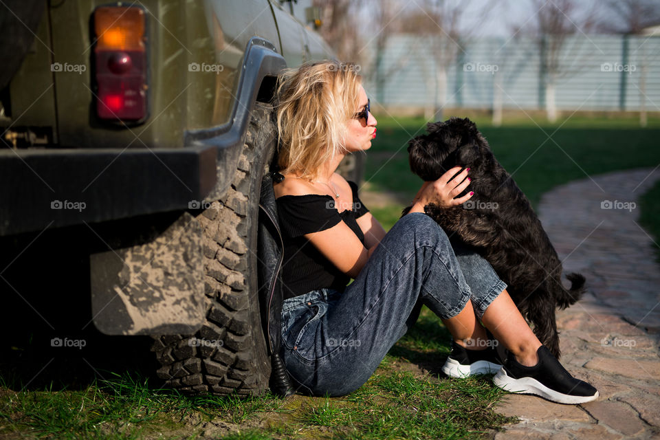 Cute blond girl near car with her black dog