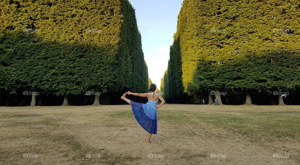 Yoga pose outdoor in the park. Green trees & blue sky. Hand to big toe pose - padangustasana. 
