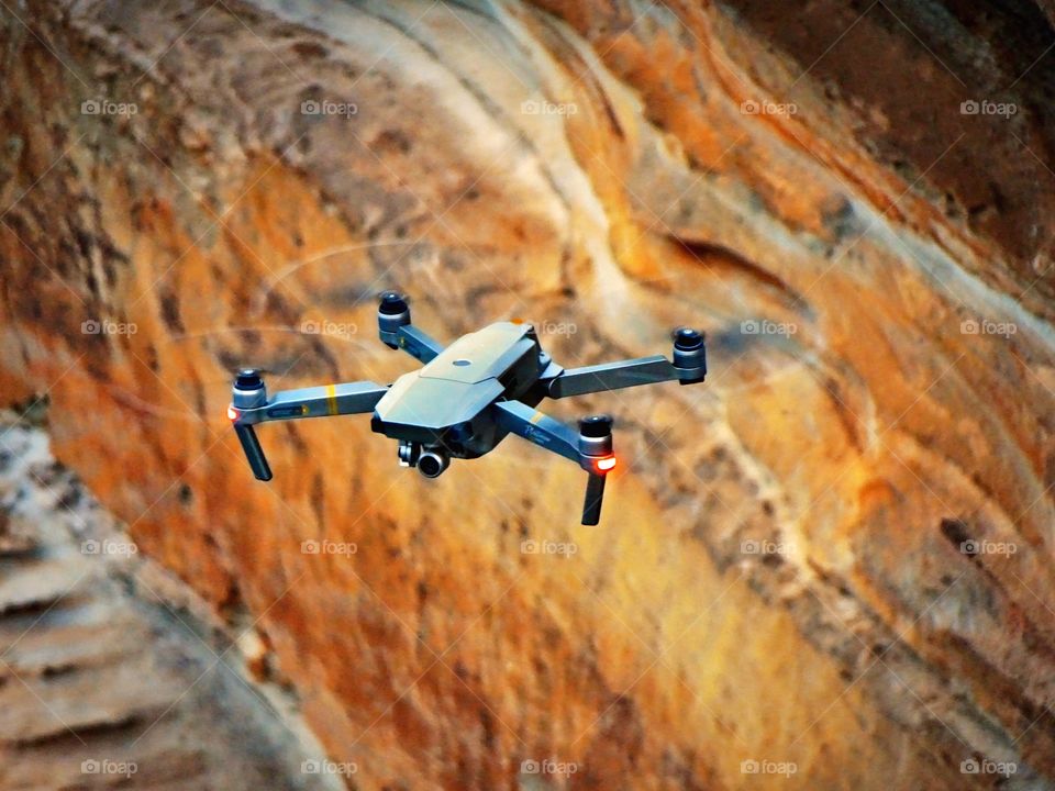 Close up of drone looking at you, flying high, against a backdrop of rocky cliffs. Beautiful colors of nature. 