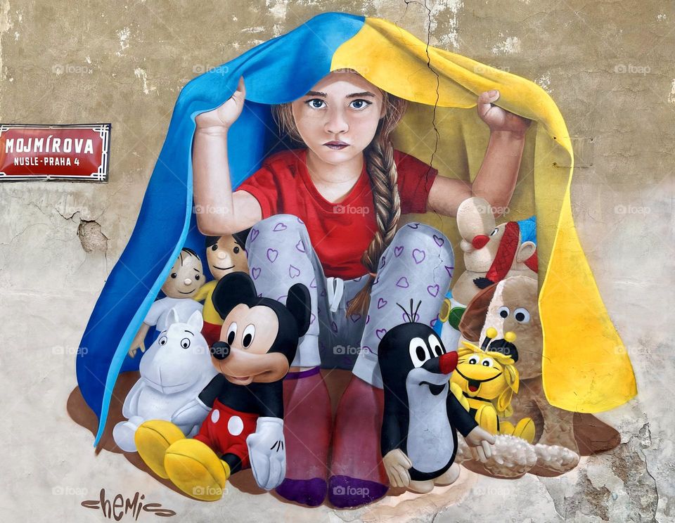 Little girl hiding her toys under Ukrainian flag. Graffiti in Prague Czech Republic 