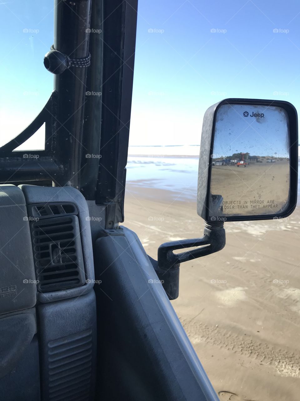 On the passenger side looking back through the mirror at the amazing ride just taken across the sandy dunes. Ahead, the ocean, with foam rolling towards us.