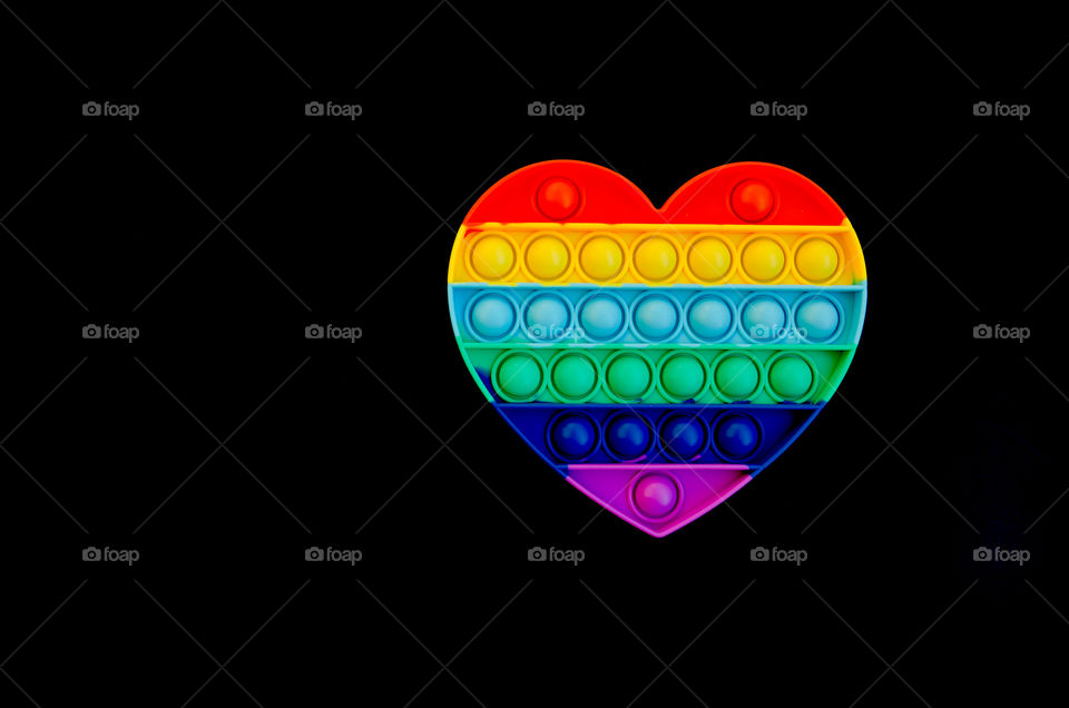 Top view of anti stress sensory toy Pop it rainbow heart on black background. Popular, trend toys in 2021.