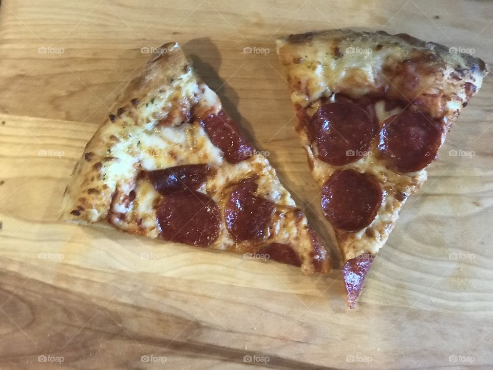 Two slices of pepperoni pizza on a cutting board 