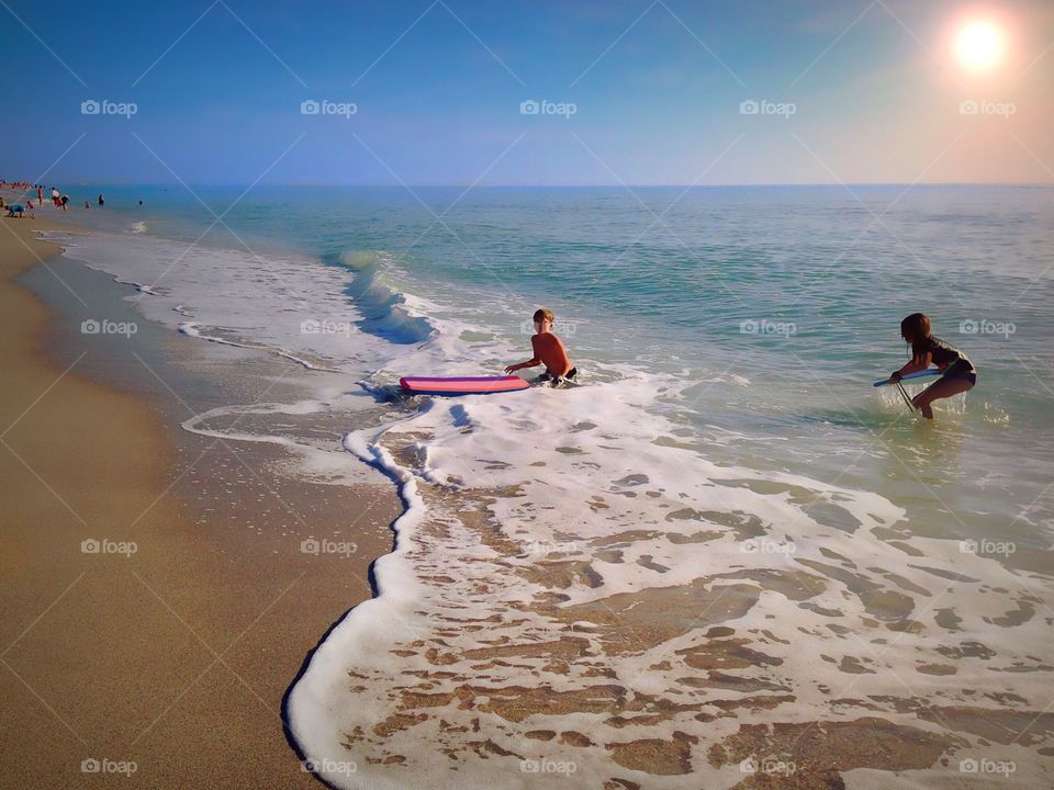 Young girl and boy riding the waves under a glowing summer sun.