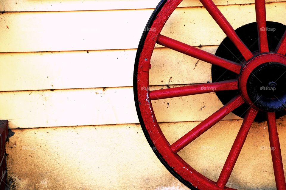 Wagon wheel sitting against the exterior of a house with yellow slats