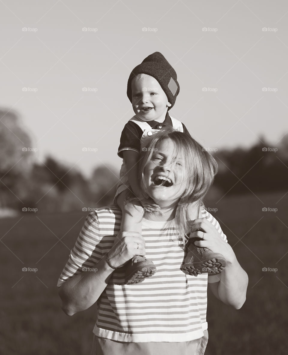 Happy mother holds her little baby boy on shoulders