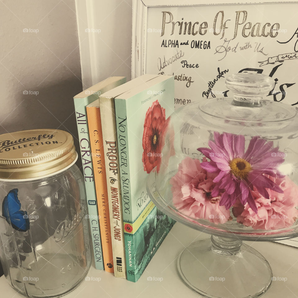 Warm light over glass decor, dome stand with flowers, standing books, Christian frame, butterfly in a jar, against a white background