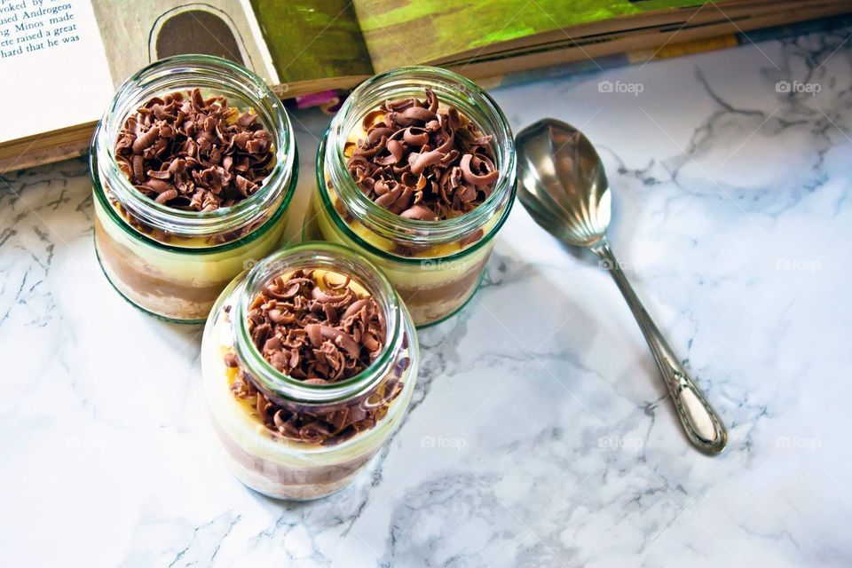 Chocolate and vanilla home-made cheesecake, served in miscellaneous jars, with a teaspoon on the side.