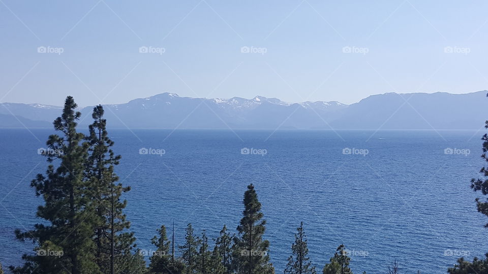 Lake Tahoe with a view of Lake and mountains with snow and a few tree tops