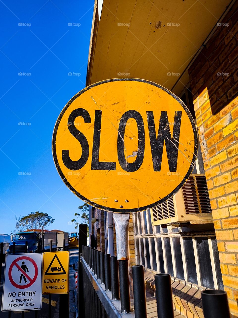 Bright yellow SLOW traffic sign at factory entrance.